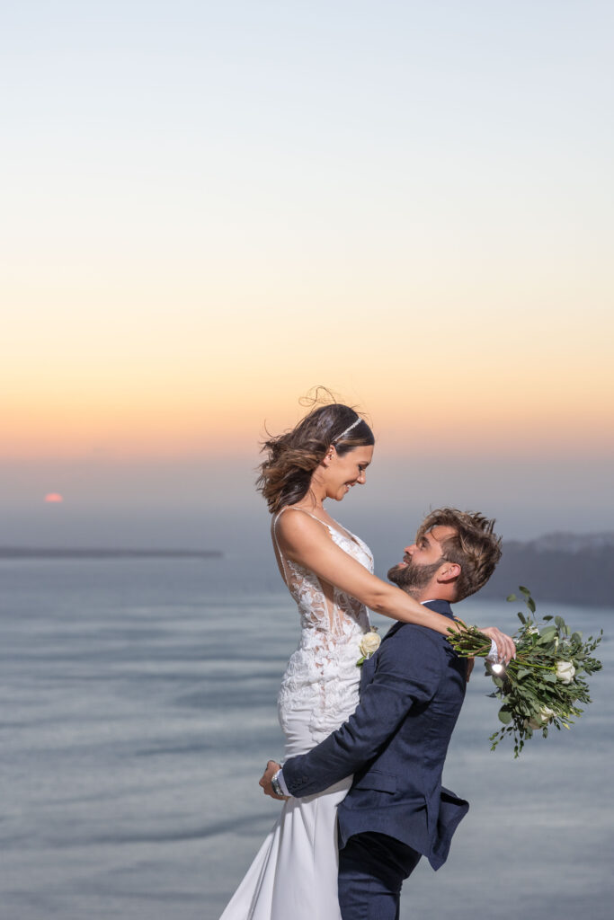 Groom lifting up bride in front of Santorini sunset