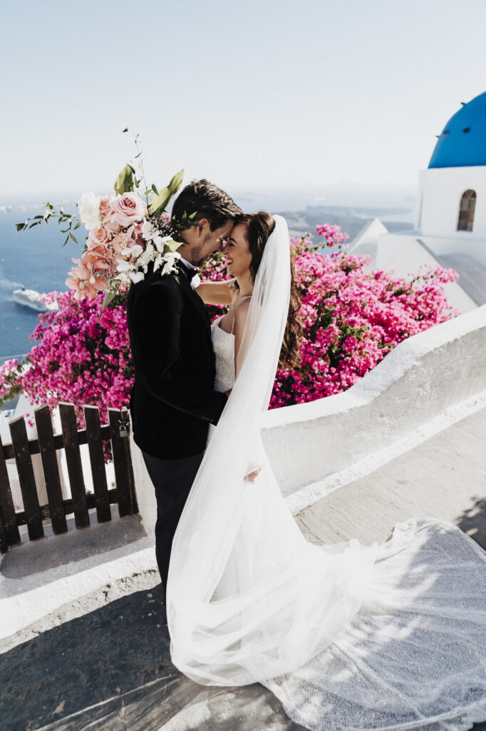 Anneliese and James kiss surrounded by pink flowers and ocean view