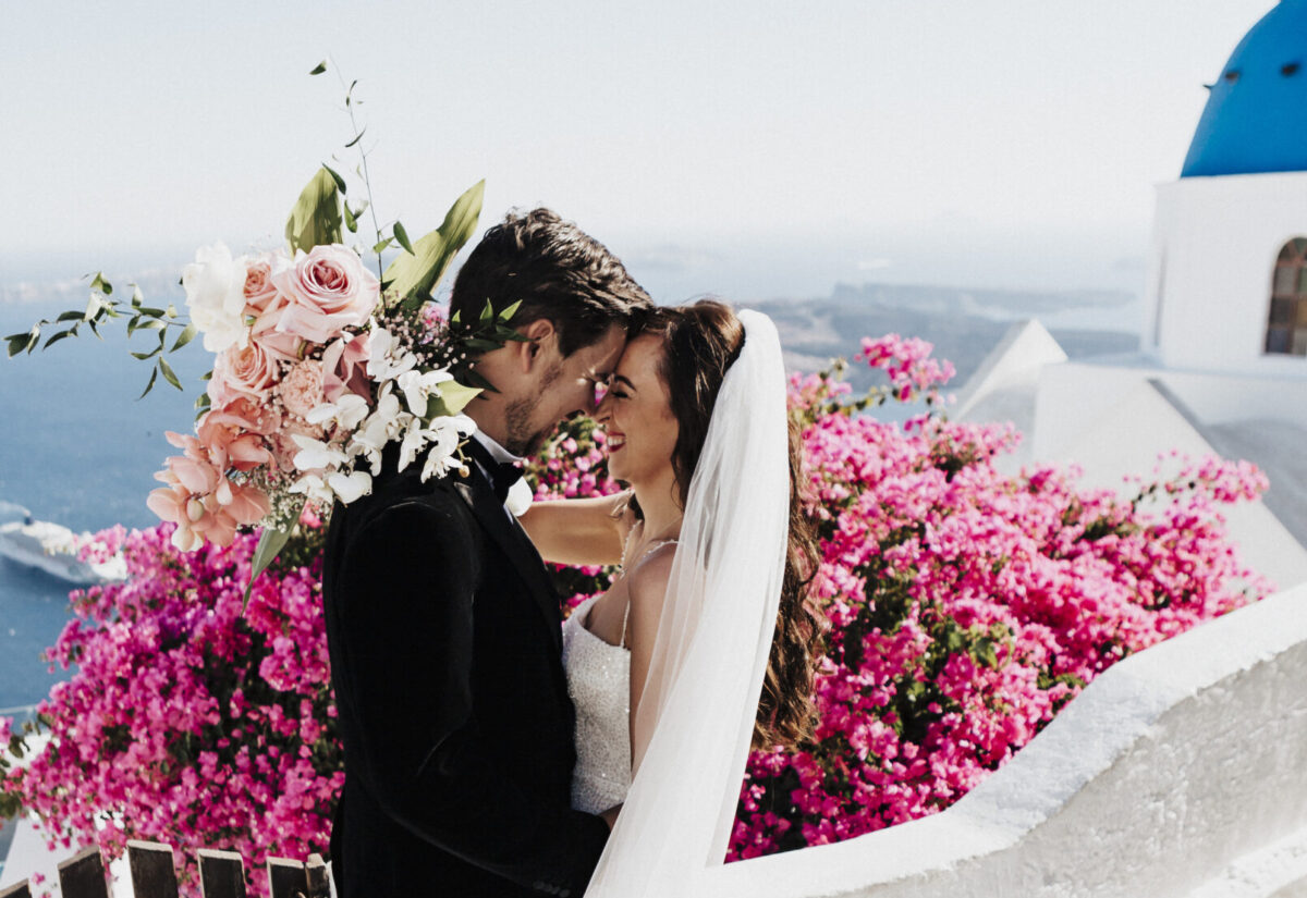 Anneliese and James kiss surrounded by pink flowers and ocean view