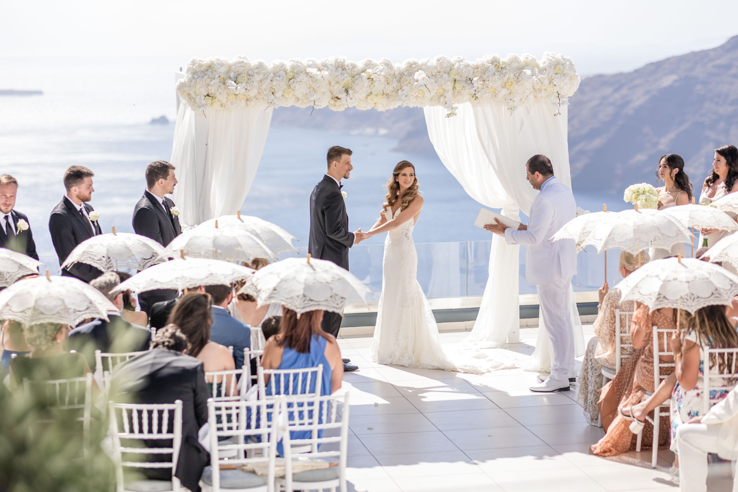 bride and groom Santorini wedding at Le Ciel with guest shoaling parasols and fans