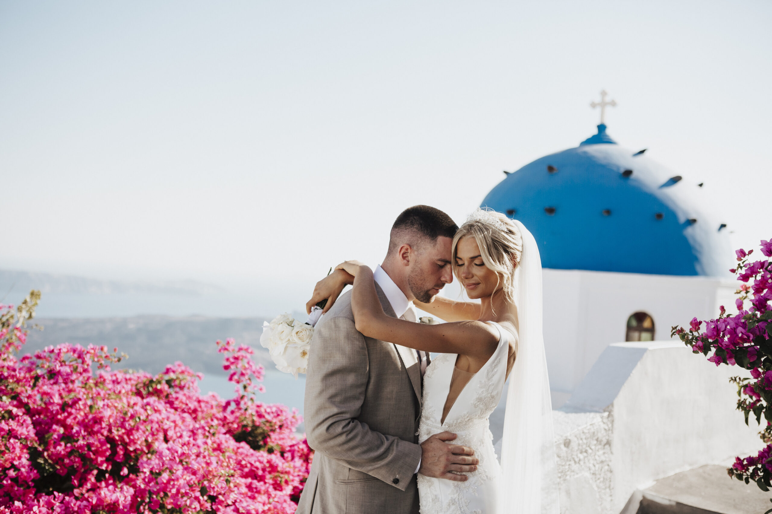 Bride and groom embracing in front of white and blue Santorini village at their destination wedding
