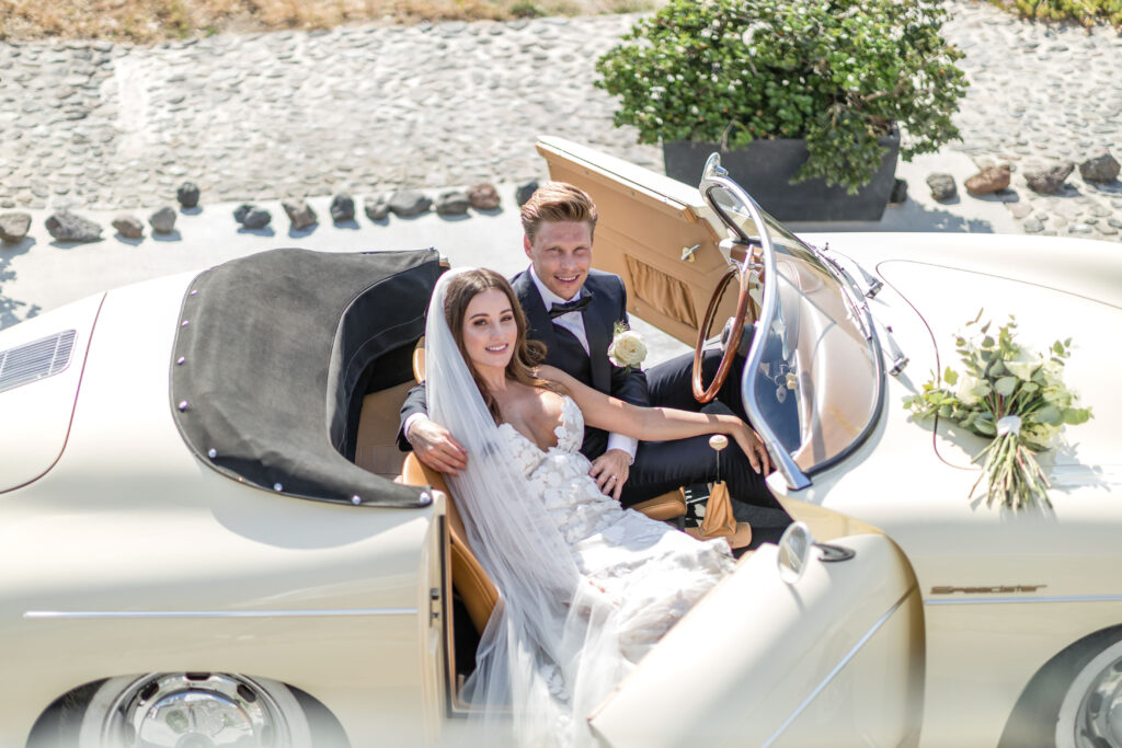 bride and groom sitting in open top vintage car at Santorini destination wedding