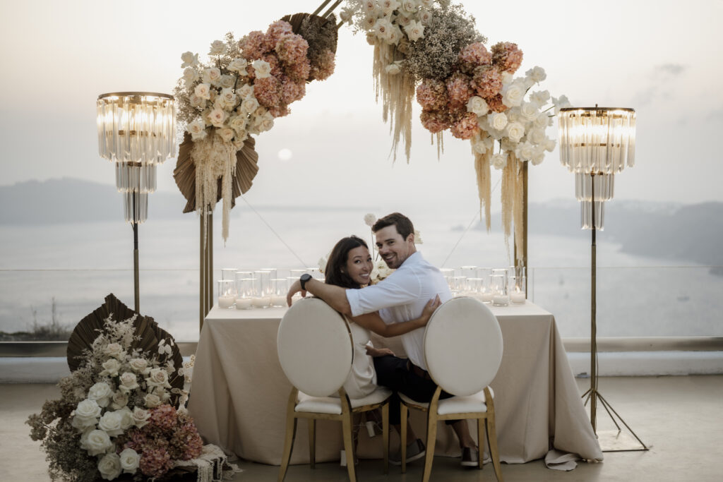 bride and groom sitting underneath floral display at Le Ciel Santorini