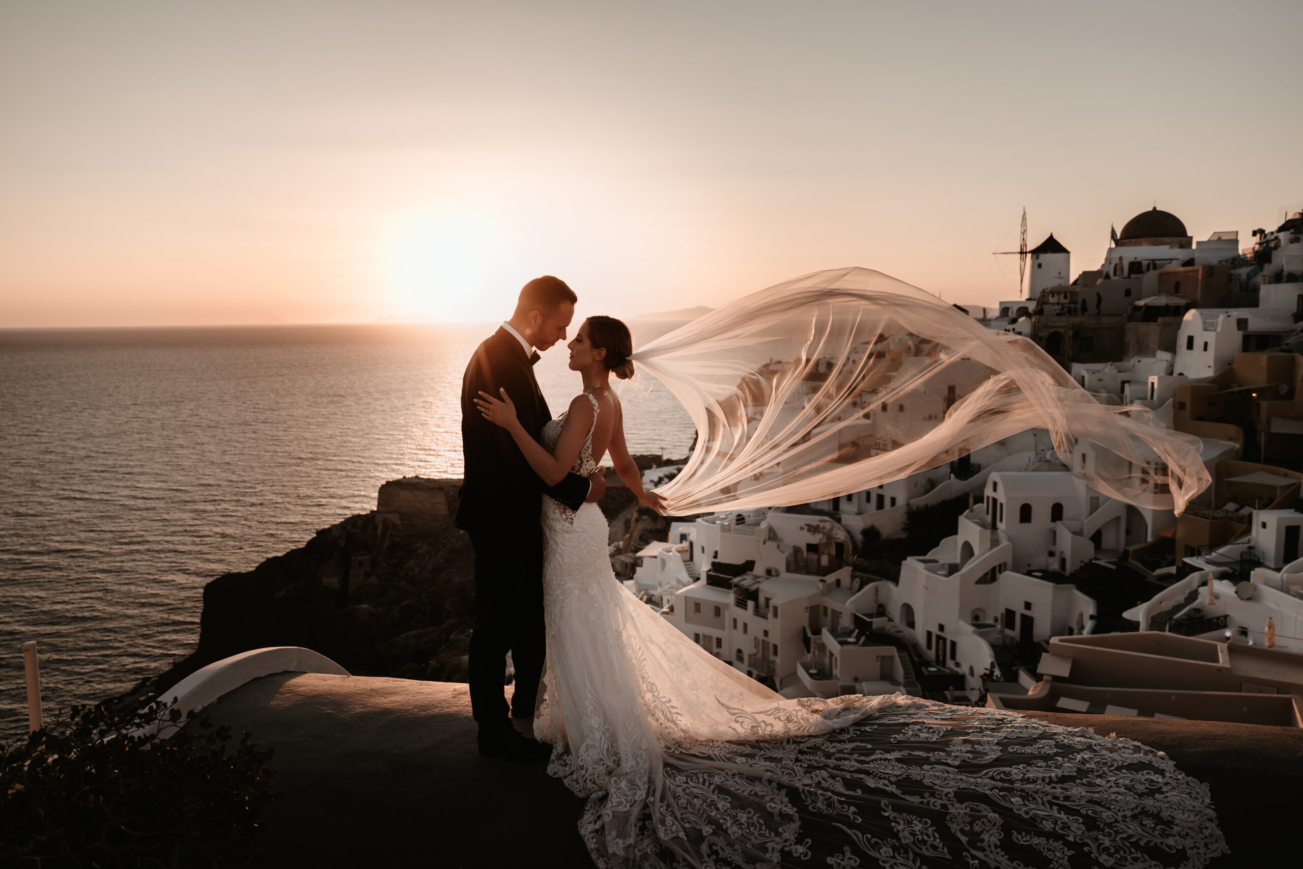 couple embracing in front of Santorini sunset on the clifftops near le Ciel