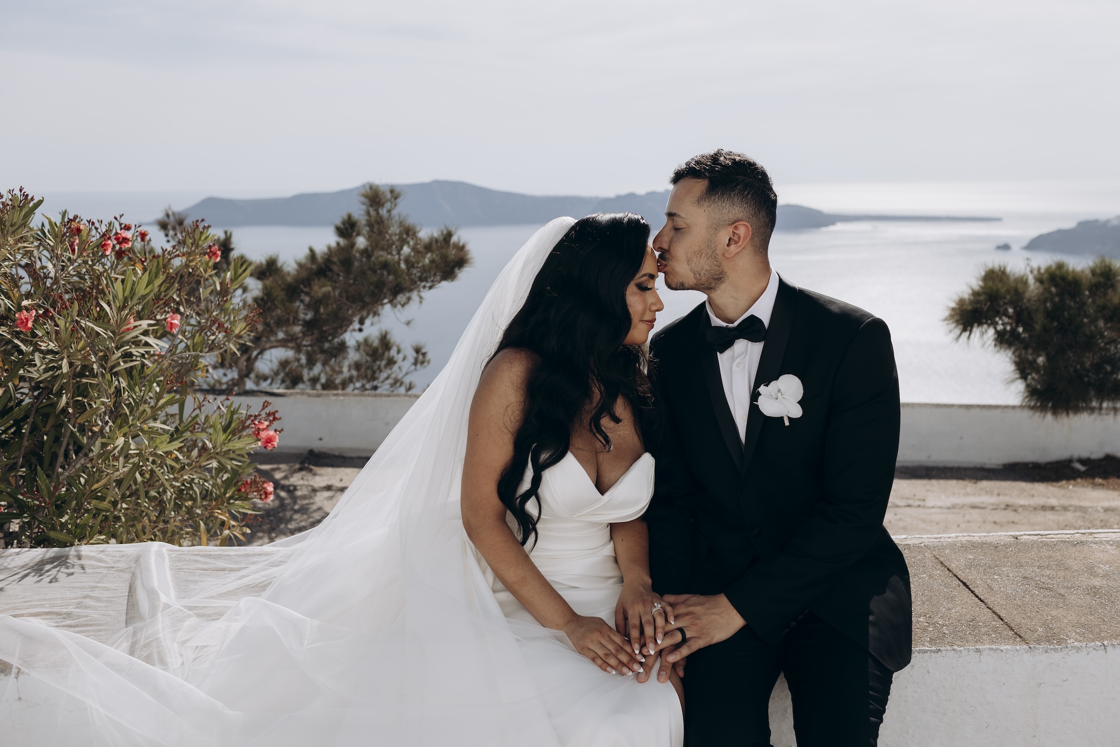 Emily and Omar kissing with Santorini sea view behind them 