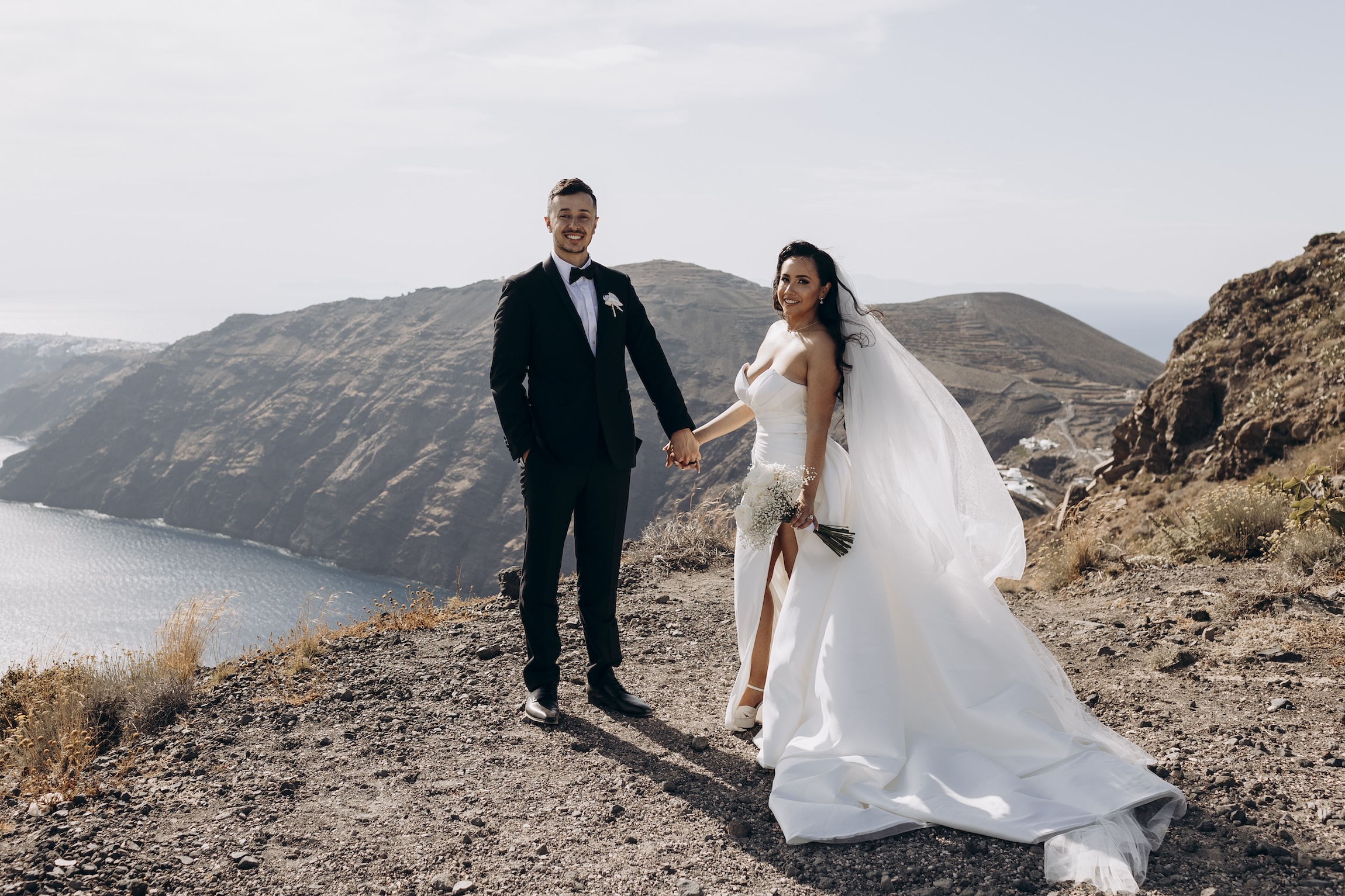 bride and groom standing on santorini clifftop after wedding