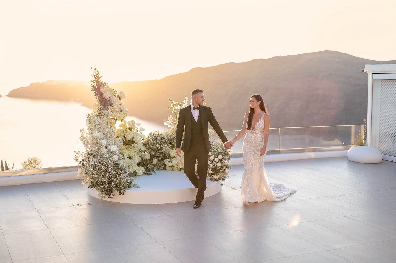 bride and groom holding hands at le Ciel Santorini wedding venue with sun setting